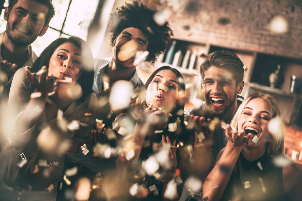 Cheerful group of people blowing confetti and smiling while enjoying party together