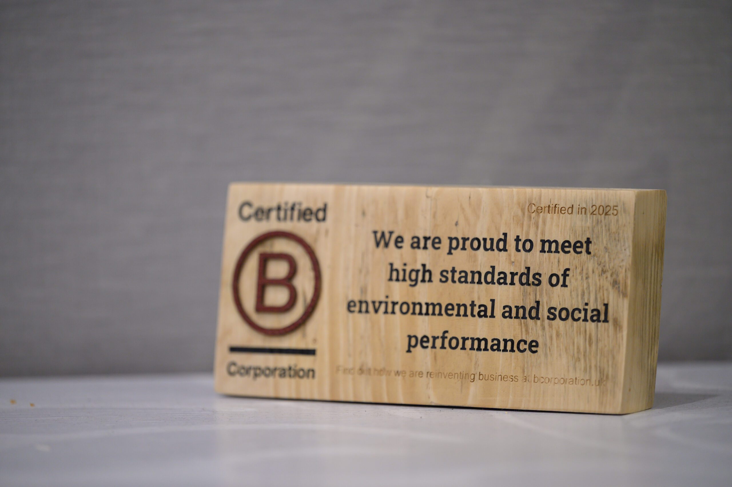 A wooden block with the B Corp logo and the words We are proud to meet high standards of environmental and social performance
