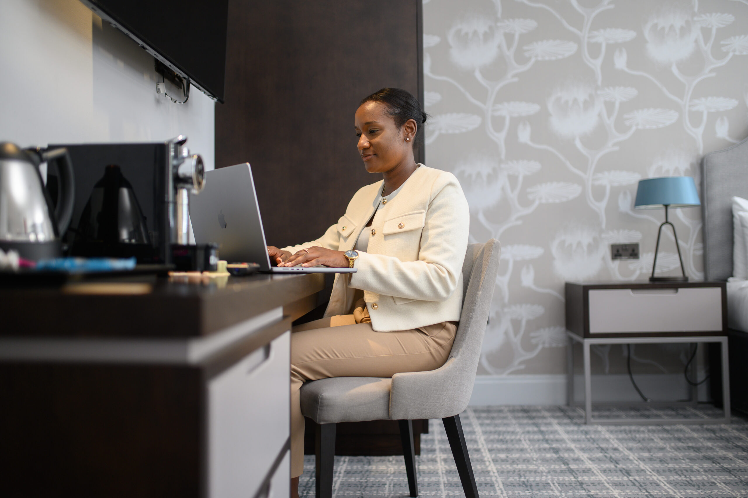 A woman sitting at a desk in her room typing on her laptop